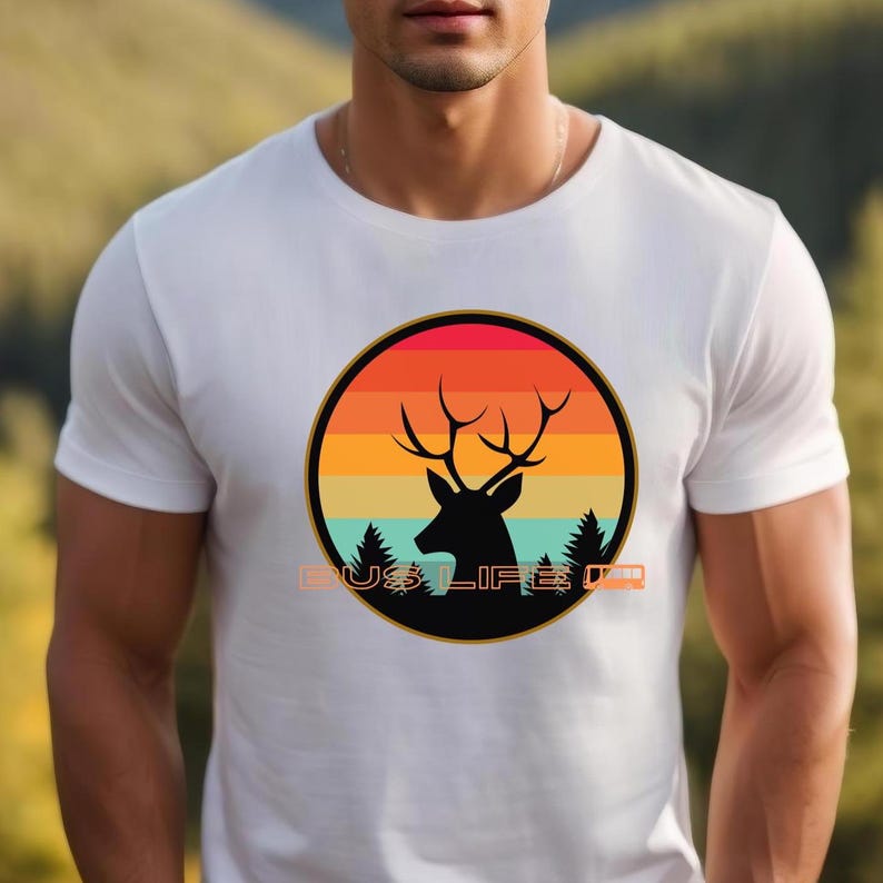 May include: White t-shirt with a circular design showing a deer silhouette against an orange, yellow, and red sunset. The design includes the text "BUS LIFE". The shirt is made of a soft material.