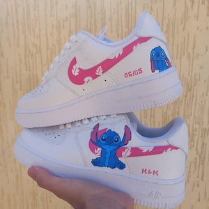 May include: White sneakers with pink accents and a cartoon character design. The sneakers feature a pink swoosh, pink leaf pattern, and a blue cartoon character on the side. The text "06/05" and "M&M" are also visible.