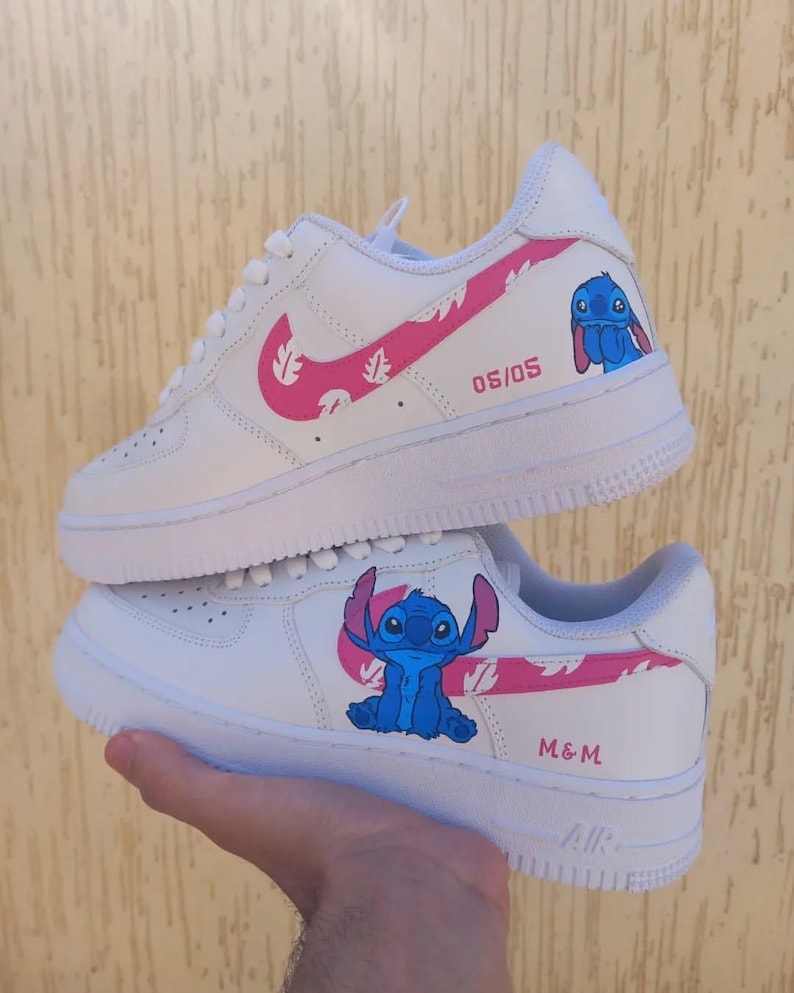 May include: White sneakers with pink accents and a cartoon character design. The sneakers feature a pink swoosh, pink leaf pattern, and a blue cartoon character on the side. The text "06/05" and "M&M" are also visible.