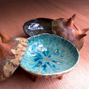 May include: A white ceramic mug with a black handle and the text "But First, Coffee" in a black, handwritten-style font. The mug is likely 4 inches tall and holds approximately 12 ounces of liquid.