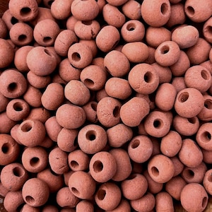 May include: Close-up of a pile of reddish-brown, donut-shaped beads. Each bead has a hole running through the center. The beads are smooth and appear to be made of a natural material.
