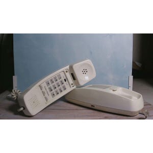 May include: A white wall-mounted telephone with a detachable handset featuring a numeric keypad, a speaker grille, and a coiled cord. The base unit has a cradle for the handset and a smooth, curved plastic exterior design for home or office use.