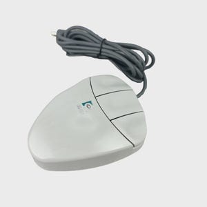May include: A light gray wired computer mouse with three buttons and a coiled gray cable. The device features a small Logitech logo printed on the top surface. The mouse has a rounded, ergonomic shape and is designed for desktop computer navigation.