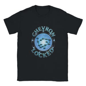 May include: A black short-sleeve t-shirt featuring a central graphic of a blue circular portal with a constellation of connected dots. The text CHEVRON LOCKED is printed in a metallic blue font, curving around the top and bottom of the portal.