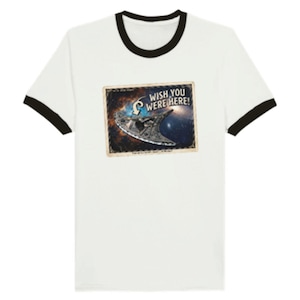 May include: A white ringer t-shirt with black trim on the collar and sleeves. The center features a rectangular graphic resembling a postcard with a space scene, a spaceship, and the text "WISH YOU WERE HERE!" printed in a bold, white font.
