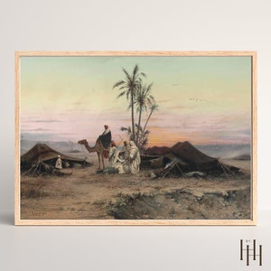 May include: A painting depicting a desert scene with a camel and people in traditional clothing. The sky is a soft pink and orange, and there are palm trees in the background. The painting is framed in a light wood frame.