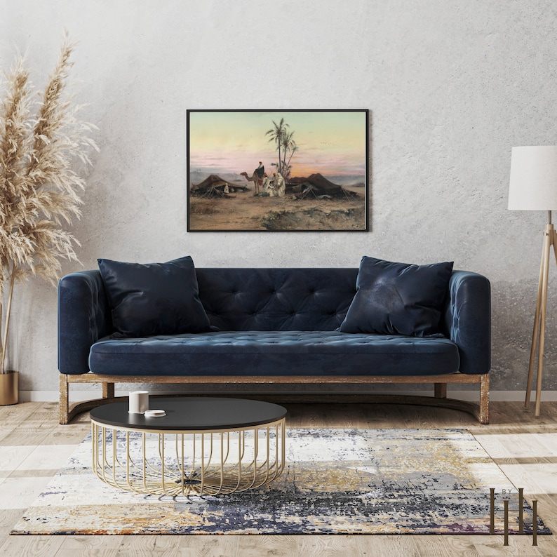 May include: A framed painting depicting a desert scene with camels and people in traditional clothing. The painting is set against a backdrop of a sunset sky with palm trees in the foreground.