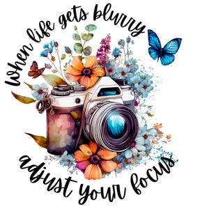 May include: A vintage camera with a blue lens surrounded by watercolor flowers and butterflies. The text "when life gets blurry adjust your focus" is written around the camera.