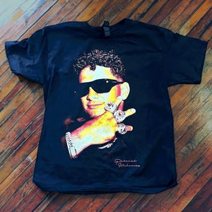 May include: Black t-shirt with a colorful image of a man wearing sunglasses and multiple rings on his fingers. The text "Patrick Mahomes" is printed on the bottom of the shirt.