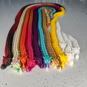 May include: A set of 12 colorful dragon tail keychains, each with a different color and design. The keychains are made of a soft, flexible material and are perfect for adding a touch of whimsy to your keys or bag.