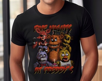 May include: Black t-shirt with a graphic print of the characters from the video game "Five Nights at Freddy's". The characters are Freddy Fazbear, Bonnie the Bunny, Chica the Chicken, Foxy the Pirate Fox, and Golden Freddy.