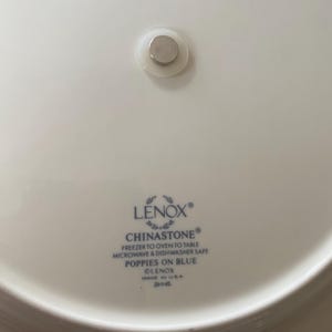 May include: A white Lenox Chinastone plate with a blue floral design, featuring the text "POPPIES ON BLUE". The plate is microwave and dishwasher safe. A small magnet is attached to the back.