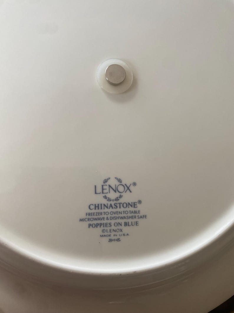 May include: A white Lenox Chinastone plate with a blue floral design, featuring the text "POPPIES ON BLUE". The plate is microwave and dishwasher safe. A small magnet is attached to the back.