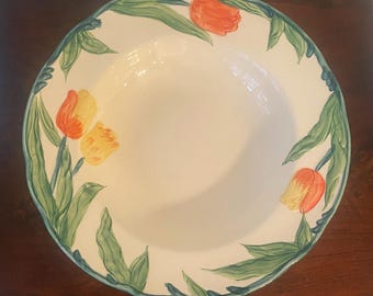 May include: A round ceramic bowl with a white interior and a wide rim featuring a hand-painted pattern of orange and yellow tulips with green leaves. The outer edge of the rim is finished with a thin, wavy green painted border.