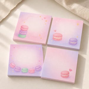 May include: Four square sticky note pads featuring a pastel pink and purple gradient background. The designs include illustrations of colorful macarons, small yellow stars, and tiny pink hearts arranged in various patterns across the paper sheets.