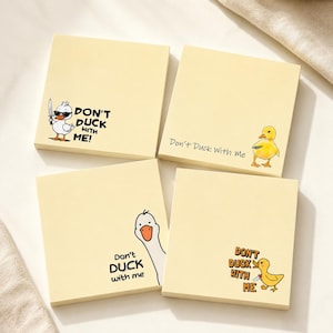 Può includere: Quattro foglietti adesivi quadrati giallo chiaro con illustrazioni di anatre in stile cartoon e il testo "DON'T DUCK WITH ME!". Un foglietto mostra un'anatra con occhiali da sole e un coltello, un altro un anatroccolo giallo, un terzo una testa d'oca e l'ultimo un'anatra con un coltello.