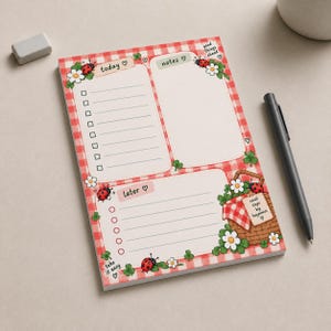 Puede incluir: Un bloc de notas rectangular con un borde de cuadros vichy rojos y blancos, que incluye secciones etiquetadas como today, notes y later. El diseño presenta ilustraciones de mariquitas, margaritas blancas, tréboles verdes y una cesta de picnic con el texto small steps big happiness.