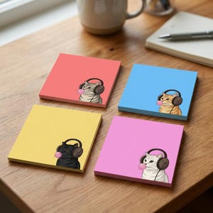 Puede incluir: Cuatro blocs de notas adhesivas cuadrados en color coral, azul, amarillo y rosa. Cada bloc presenta una pequeña ilustración de un gato con orejeras marrones soplando una burbuja de chicle rosa. Los gatos son gris atigrado, naranja, negro y blanco.