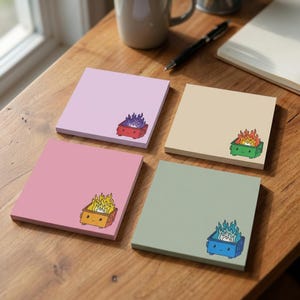 May include: Four square sticky note pads in light purple, beige, pink, and sage green. Each pad features a small, smiling dumpster illustration in the bottom right corner, with flames in purple, orange, yellow, and blue rising from the containers.