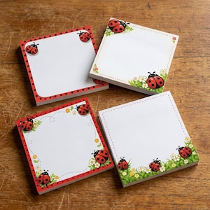 Puede incluir: Cuatro blocs de notas adhesivas cuadrados con ilustraciones de mariquitas. Cada bloc tiene un centro blanco con detalles en rojo, verde y amarillo, incluyendo mariquitas, pequeñas flores y bordes punteados o discontinuos. Los diseños varían.