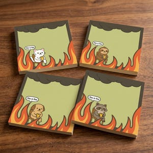 May include: Four square sticky note pads featuring a light green background with orange flames at the bottom and dark gray smoke at the top. Each pad shows a different animal sitting in a chair holding a mug with the text This is fine.