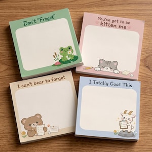 Peut inclure: Quatre blocs de notes adhésives carrés avec des illustrations d'animaux et du texte. Le bloc vert dit Don't Froget avec une grenouille, le rose You've got to be kitten me avec un chat, le beige I can't bear to forget avec un ours, et le bleu I Totally Goat This avec une chèvre.