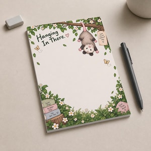 以下が含まれることがあります： 木の枝にぶら下がったオポッサムのイラストと「Hanging In There」という文字が描かれた長方形のメモ帳。緑の葉、白い花、蝶、そして「Small Steps」「Brighter Days」「You Got This」と書かれた本の積み重ねがデザインされています。