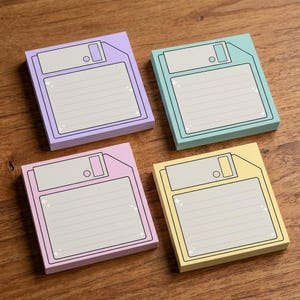 Può includere: Quattro blocchetti di foglietti adesivi quadrati in viola pastello, verde acqua, rosa e giallo. Ogni blocchetto presenta una grafica stampata di un floppy disk vintage con un'area etichetta grigio chiaro, righe e piccole stelle bianche.