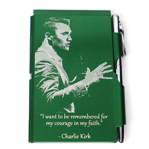 May include: Green notebook with a portrait and quote by Charlie Kirk. The notebook has a pen holder with a silver pen. The quote reads, "I want to be remembered for my courage in my faith."