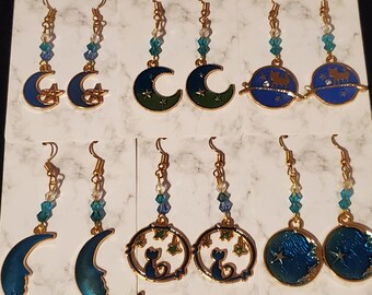 May include: Ten pairs of gold tone earrings with blue and green enamel. The earrings feature crescent moons, stars, and cats.