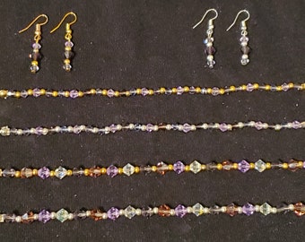 May include: Four beaded bracelets with gold and silver accents and a pair of earrings with purple and clear crystals.
