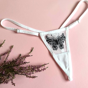 Op de afbeelding: Witte lingerie met een zwarte vlinderborduursel. De lingerie heeft verstelbare bandjes en een delicate mesh stof.