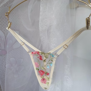 May include: Delicate white lingerie with floral embroidery in shades of pink, green, and blue. The lingerie features adjustable straps and a delicate floral pattern.