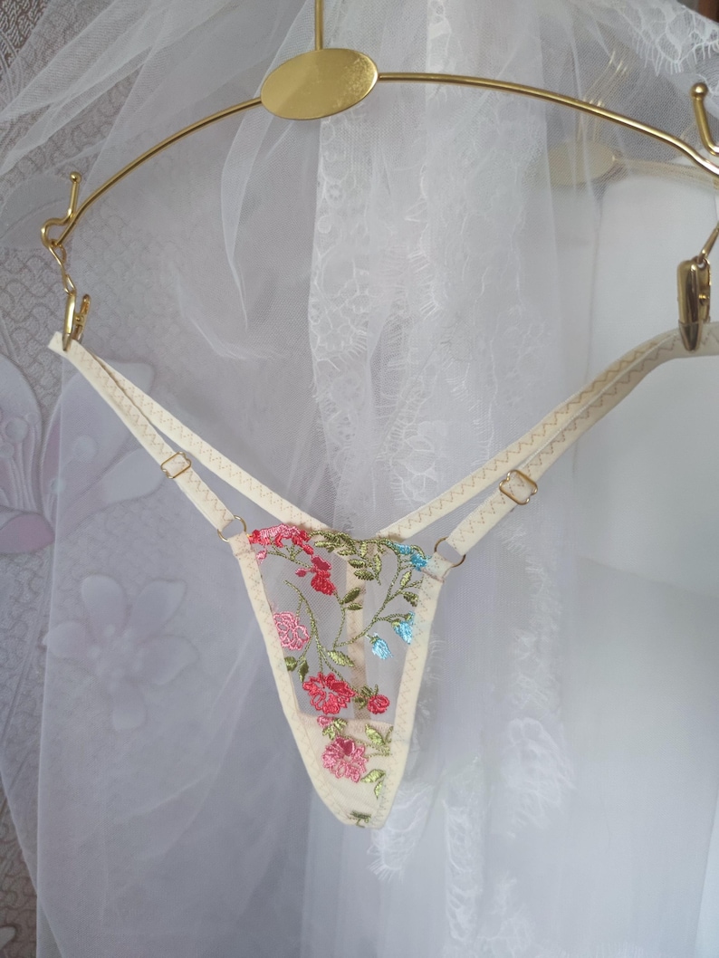 May include: Delicate white lingerie with floral embroidery in shades of pink, green, and blue. The lingerie features adjustable straps and a delicate floral pattern.