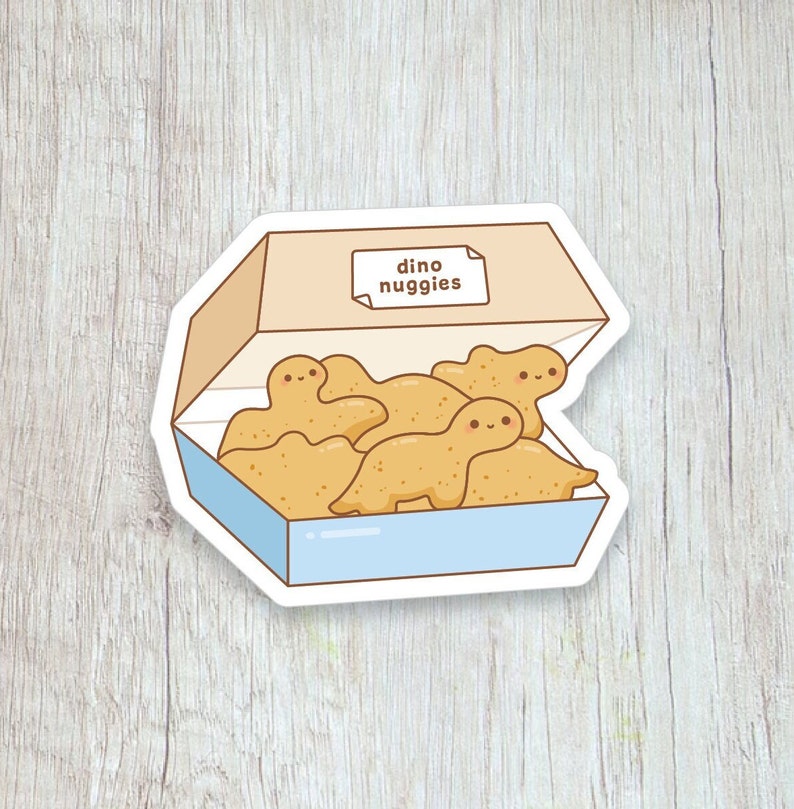 Peut inclure: Un autocollant repr&eacute;sentant une bo&icirc;te de p&eacute;pites de poulet en forme de dinosaures. Les p&eacute;pites sont brun dor&eacute; avec des visages souriants. La bo&icirc;te est bleu clair avec un dessus beige et les mots "dino nuggies" sur une &eacute;tiquette.