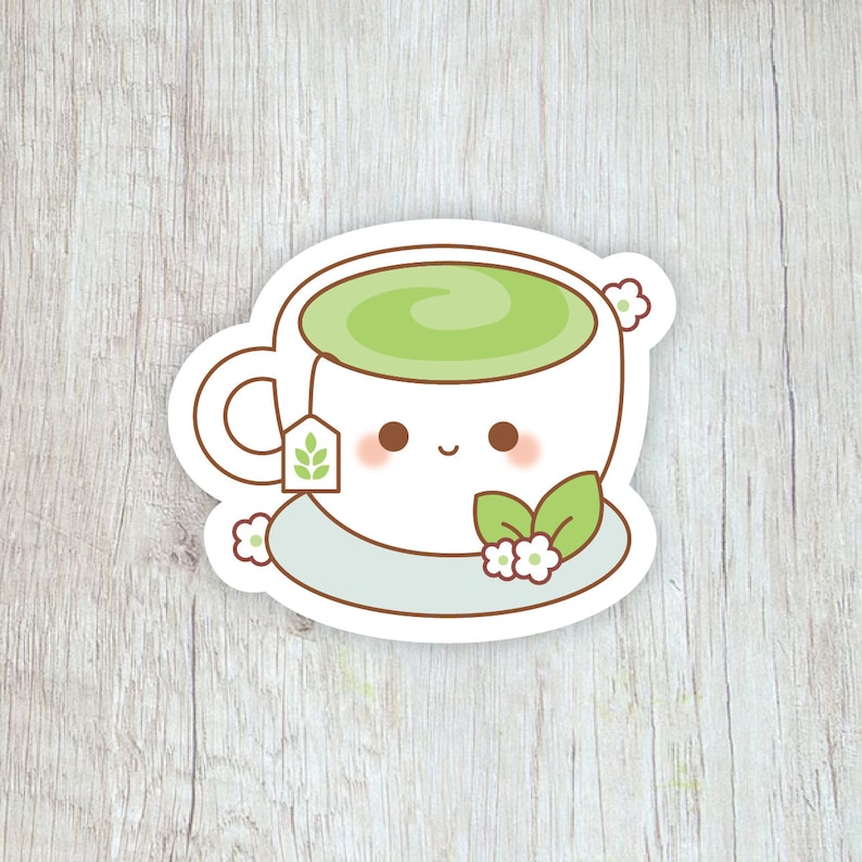Pode incluir: Um autocolante branco com uma ch&aacute;vena de ch&aacute; de desenho animado sorridente, cheia de ch&aacute; verde, com um saquinho de ch&aacute;, flores e folhas. O autocolante est&aacute; sobre um fundo claro com gr&atilde;o de madeira.