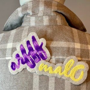 Peut inclure: Une chemise en flanelle à carreaux bruns et blancs avec deux patchs brodés. Le patch du haut est violet et dit "right", le patch du bas est jaune et dit "male".