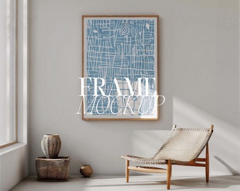 Könnte beinhalten: Ein gerahmter Kunstdruck mit einem blau-weißen abstrakten Design hängt an einer hellgrauen Wand. Der Text "FRAME MOCKUP" ist auf dem Kunstwerk überlagert. Ein Holzstuhl mit gewebter Sitzfläche und dekorative Vasen befinden sich im Raum.