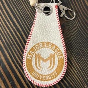 May include: A white leather keychain with a baseball stitch design and the words "MAJOR LEAGUE UNIVERSITY" in a gold circle. It has a silver clasp and a small wooden baseball bat attached.