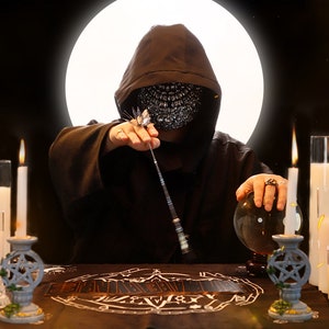 May include: A hooded figure wearing a face mask sits at a table with a crystal ball, candles, and tarot cards. The figure holds a wand in one hand and a crystal ball in the other. The background is dark with a bright white circle.