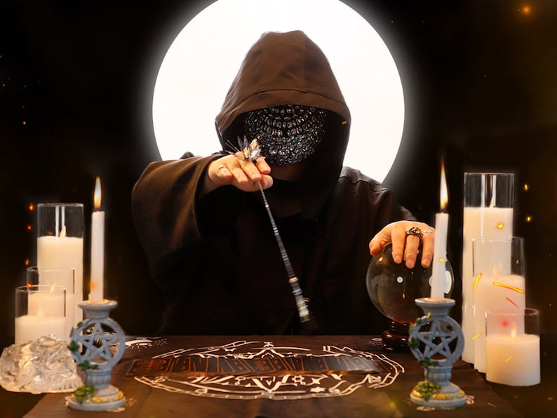 May include: A hooded figure wearing a face mask sits at a table with a crystal ball, candles, and tarot cards. The figure holds a wand in one hand and a crystal ball in the other. The background is dark with a bright white circle.
