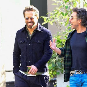 Puede incluir: Dos hombres, uno con una chaqueta vaquera azul oscuro y gafas de sol, y el otro con una camisa de cuadros verde y negro sobre una camiseta negra y pantalones vaqueros azules, caminan y hablan.