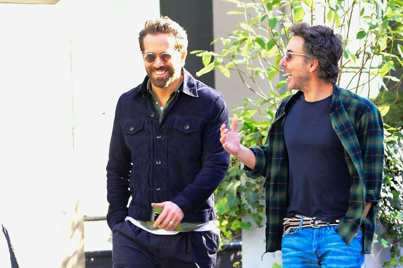 Puede incluir: Dos hombres, uno con una chaqueta vaquera azul oscuro y gafas de sol, y el otro con una camisa de cuadros verde y negro sobre una camiseta negra y pantalones vaqueros azules, caminan y hablan.