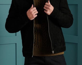 May include: A black suede jacket with a classic collar and a silver-toned metal zipper closure, worn over an olive green cable-knit sweater and paired with dark trousers. The jacket features long sleeves and a structured fit with a clean finish.