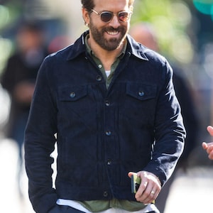Puede incluir: Un hombre con una chaqueta de gamuza azul oscuro, una camiseta verde y pantalones azul oscuro. Est&aacute; sonriendo y lleva gafas de sol.