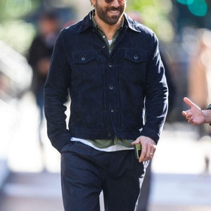 Puede incluir: Un hombre con una chaqueta de pana azul oscuro, una camiseta verde y pantalones azul oscuro. Est&aacute; sonriendo y lleva gafas de sol.