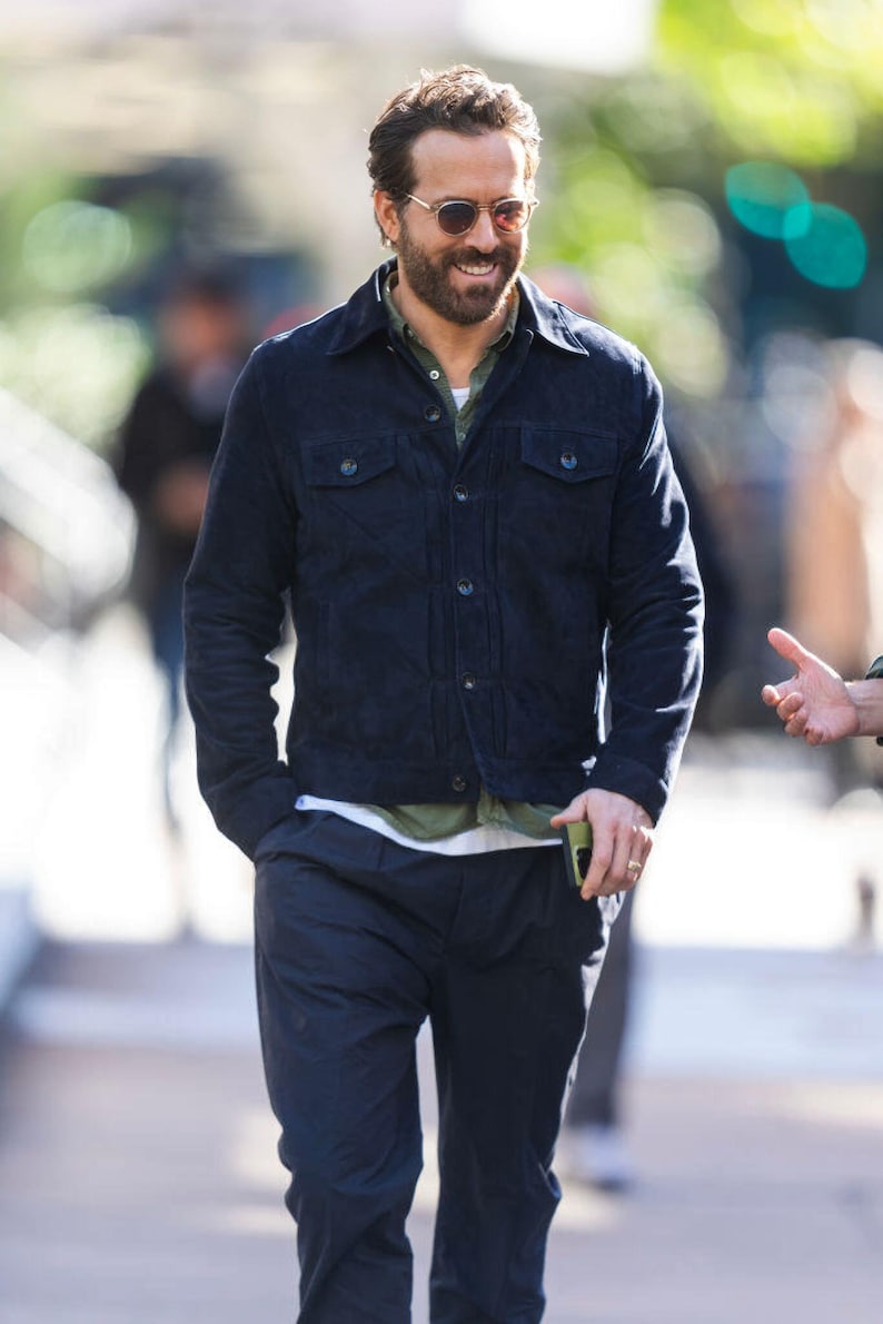 Puede incluir: Un hombre con una chaqueta de pana azul oscuro, una camiseta verde y pantalones azul oscuro. Est&aacute; sonriendo y lleva gafas de sol.