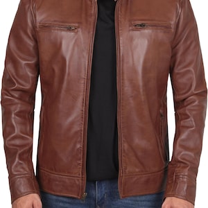 Puede incluir: Chaqueta de cuero marrón con cremallera, dos bolsillos en el pecho y cuello alzado. La chaqueta se lleva sobre una camiseta negra y vaqueros azules.