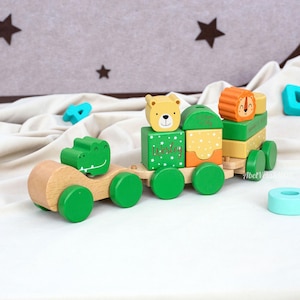 May include: Wooden toy train with animal-shaped blocks. The train features a green alligator, a bear, and a lion. The blocks are painted in green, yellow, and orange with the name "Wesley" on one block. The train is made of natural wood and green wheels.