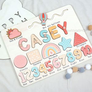 May include: Wooden educational puzzle featuring the name "CASEY" in colorful letters, along with shapes, numbers, and a rainbow design. Includes a hot air balloon and the words "Sun & Cloud".